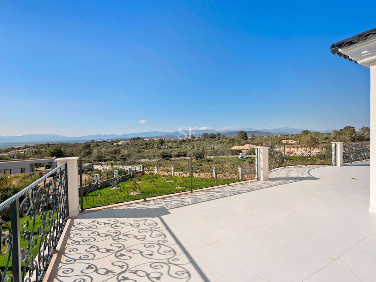 Terraza con suelo color crema y barandilla de hierro forjado con vistas a un valle verde y montañas.