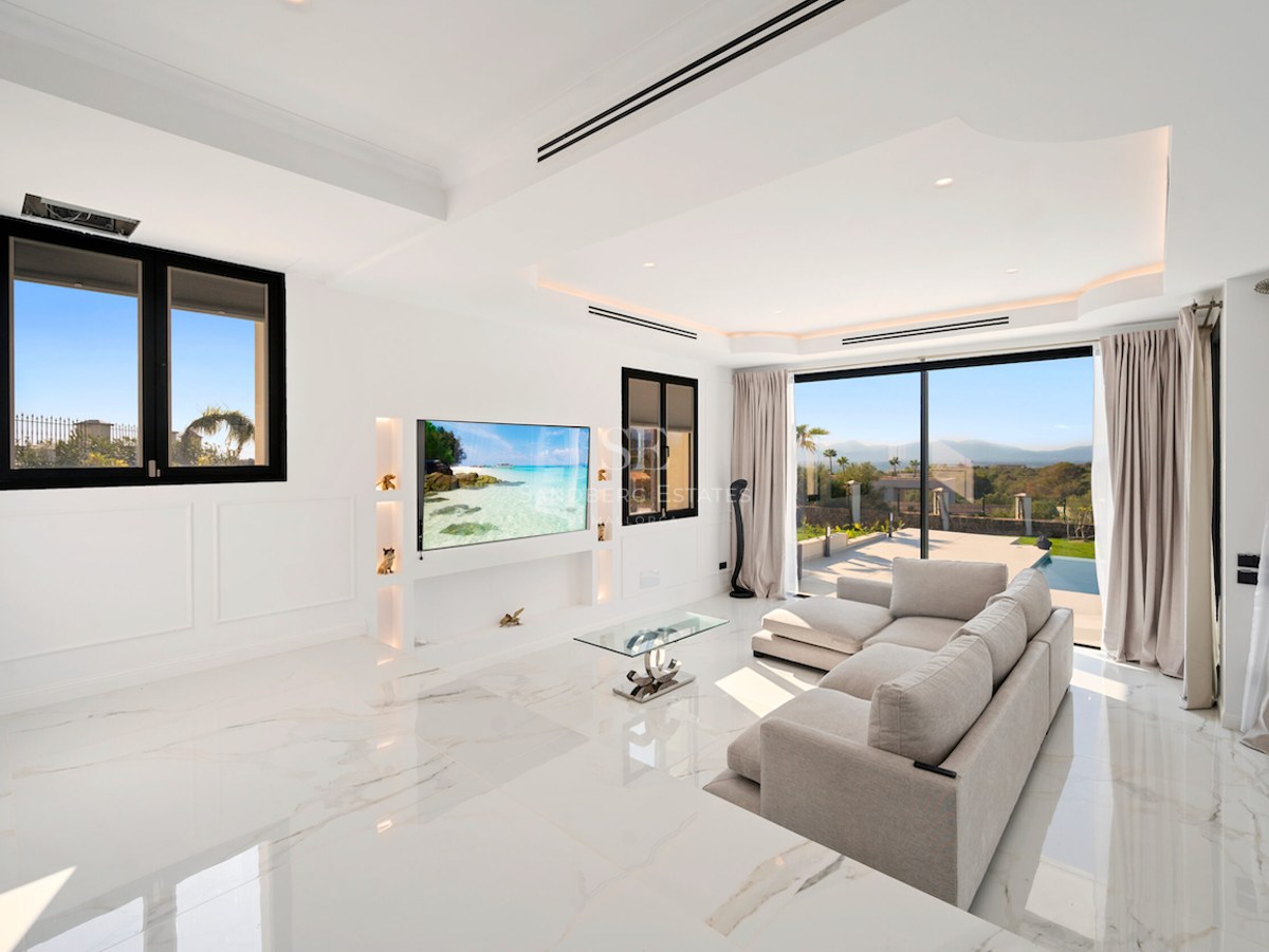 Salón contemporáneo luminoso con suelos de mármol blanco, grandes puertas correderas de cristal y TV de pared.