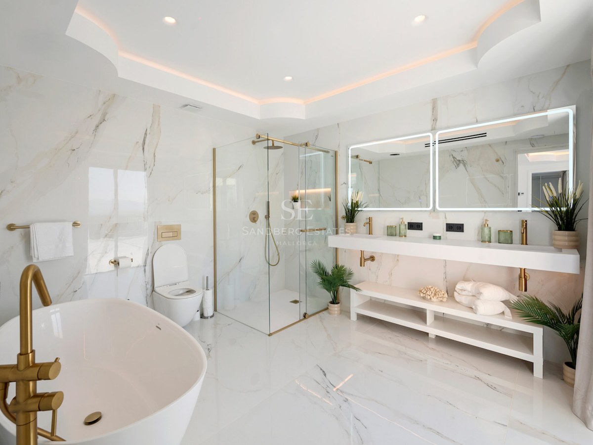 Baño de lujo con paredes de mármol, grifería dorada, bañera exenta, ducha de cristal y lavabo doble.