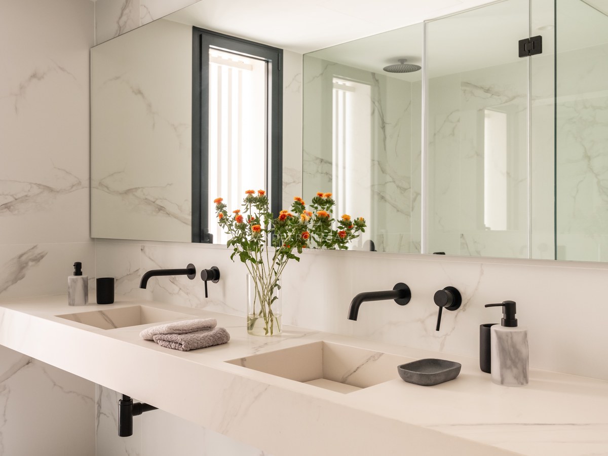Modern master bathroom featuring a double marble vanity, integrated sinks, matte black faucets, and large wall mirror.
