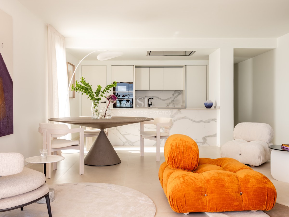 Bright open-plan living room and kitchen featuring an orange velvet sofa, marble backsplashes, and a round dining table.