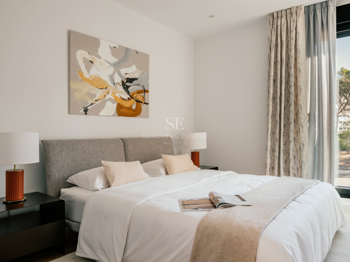 Chambre moderne avec tête de lit grise, linge blanc, art abstrait et grande baie vitrée.