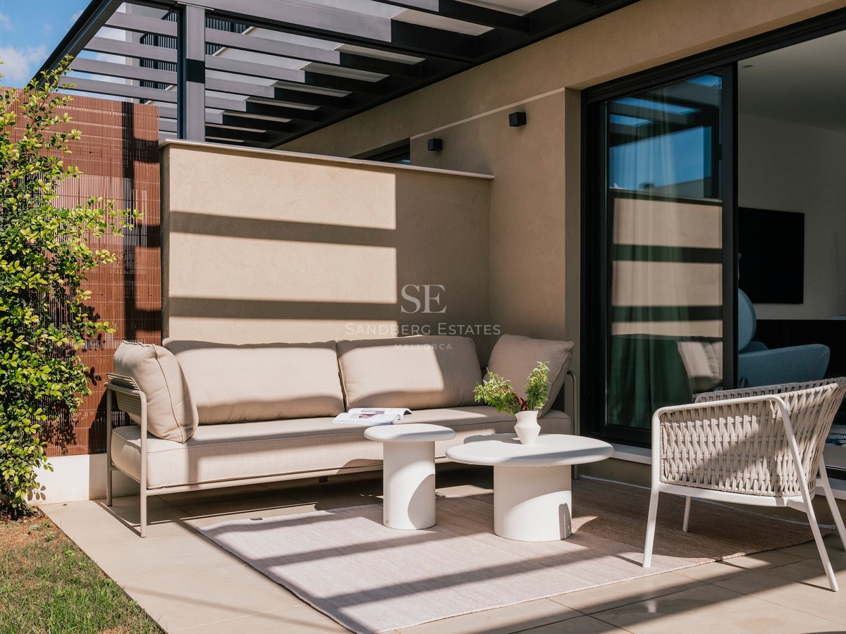 Terrasse moderne avec canapé beige, tables basses blanches et fauteuil tressé sous une pergola architecturale.