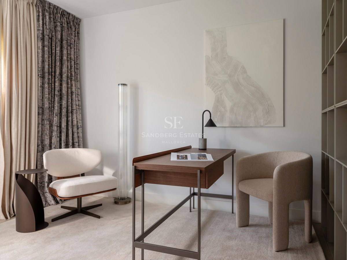 Bureau moderne avec table en noyer, fauteuil beige sculptural et œuvre d'art texturée dans une pièce lumineuse.