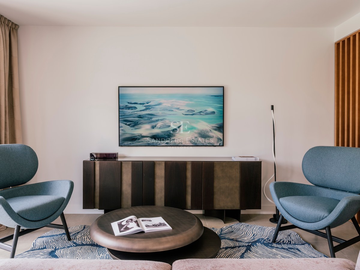 Deux fauteuils bleu canard face à une table basse en bronze et un buffet en bois sombre dans une pièce lumineuse.