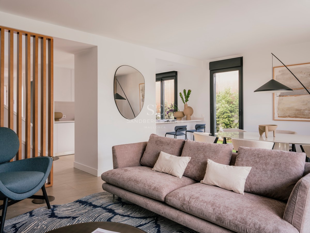 Salon moderne avec canapé mauve, fauteuil bleu, cloison en bois et espace salle à manger avec vue sur le jardin.