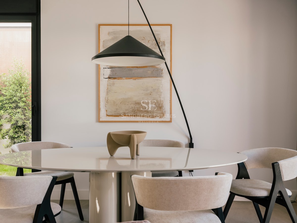 Une table à manger ronde blanche avec six chaises en tissu beige sous une suspension design noire.