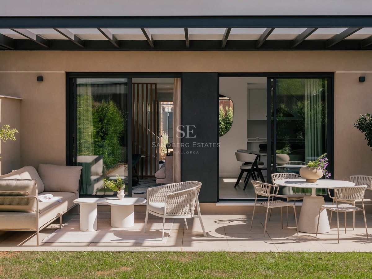 Terrasse contemporaine avec canapé beige, chaises tressées et pergola noire s'ouvrant sur le jardin.