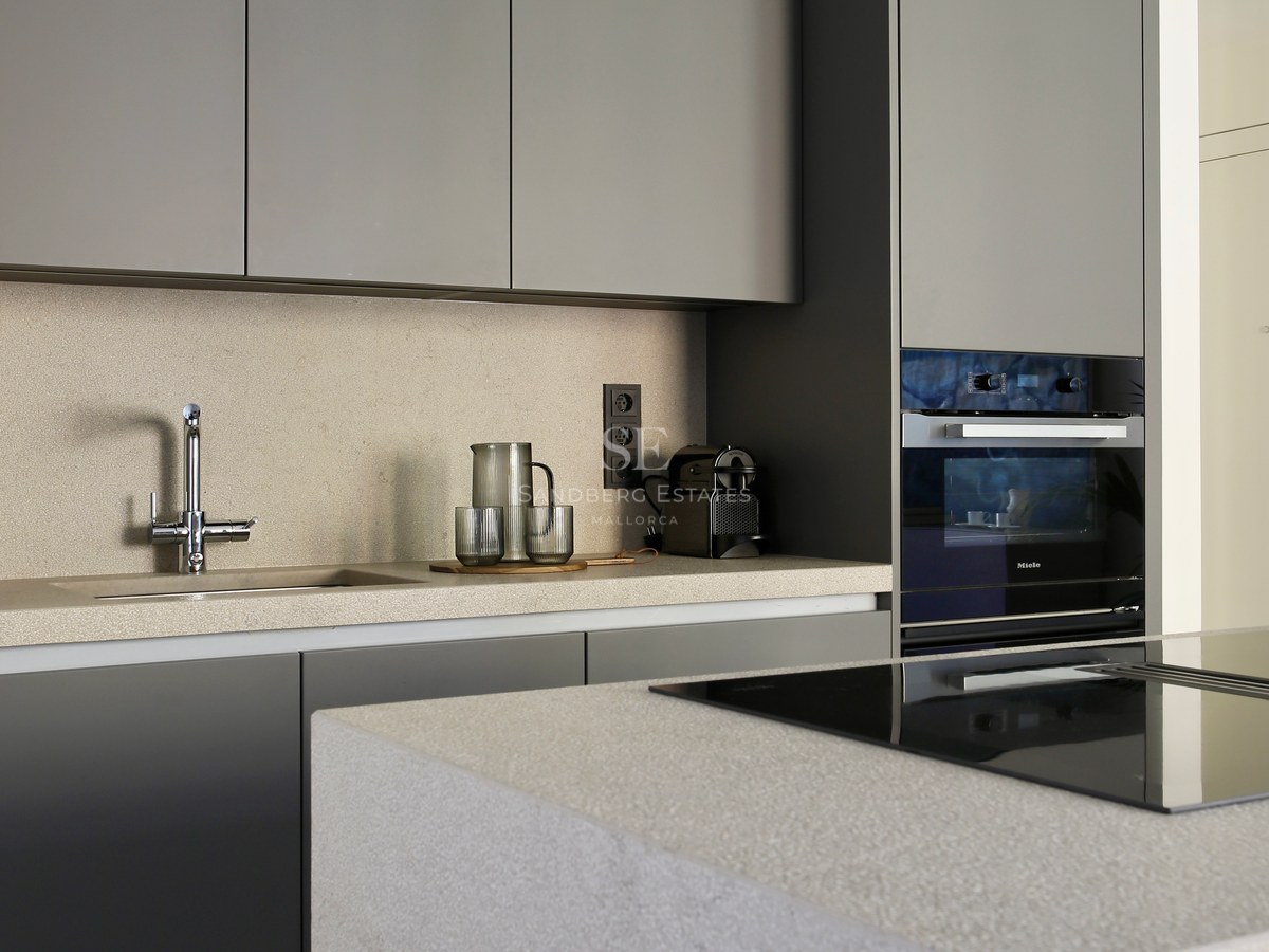 Minimalist kitchen featuring matte grey cabinetry, sand-colored stone countertops, and an integrated Miele oven.