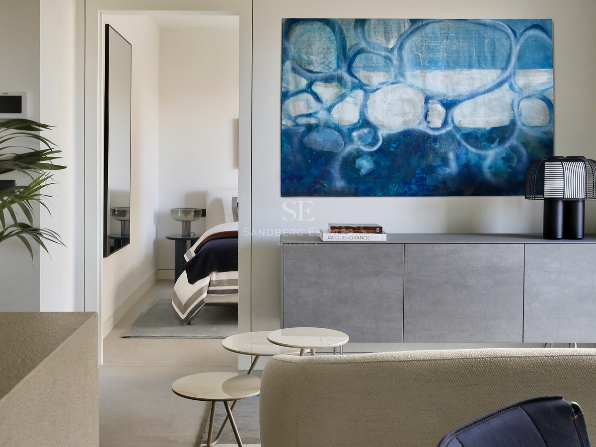 Modern living room with a large blue abstract painting over a grey sideboard, looking into a minimalist bedroom.