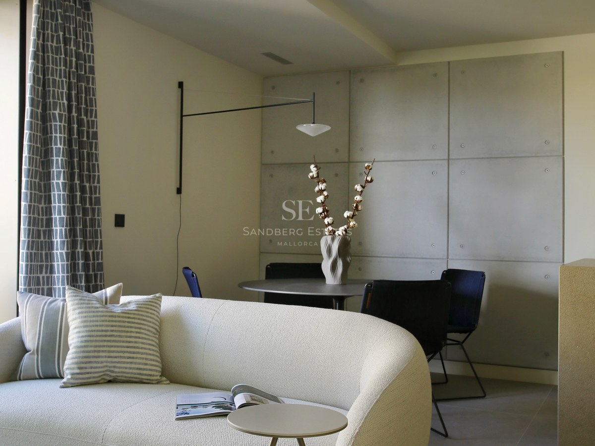 Modern living room featuring a curved white bouclé sofa, marble coffee tables, and a concrete-paneled accent wall.