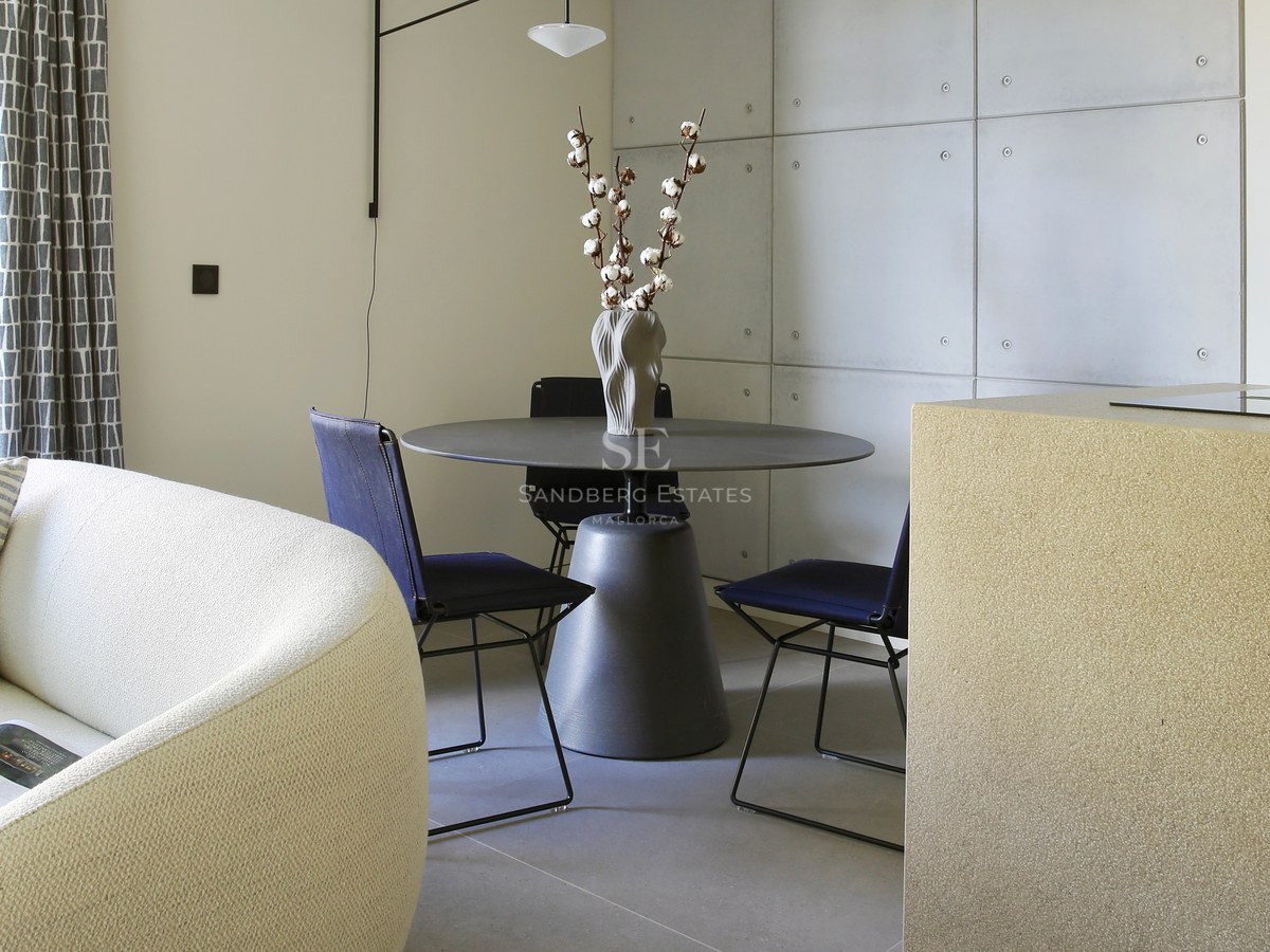 Modern dining space featuring a round table, navy chairs, and concrete panel wall next to a curved bouclé sofa.