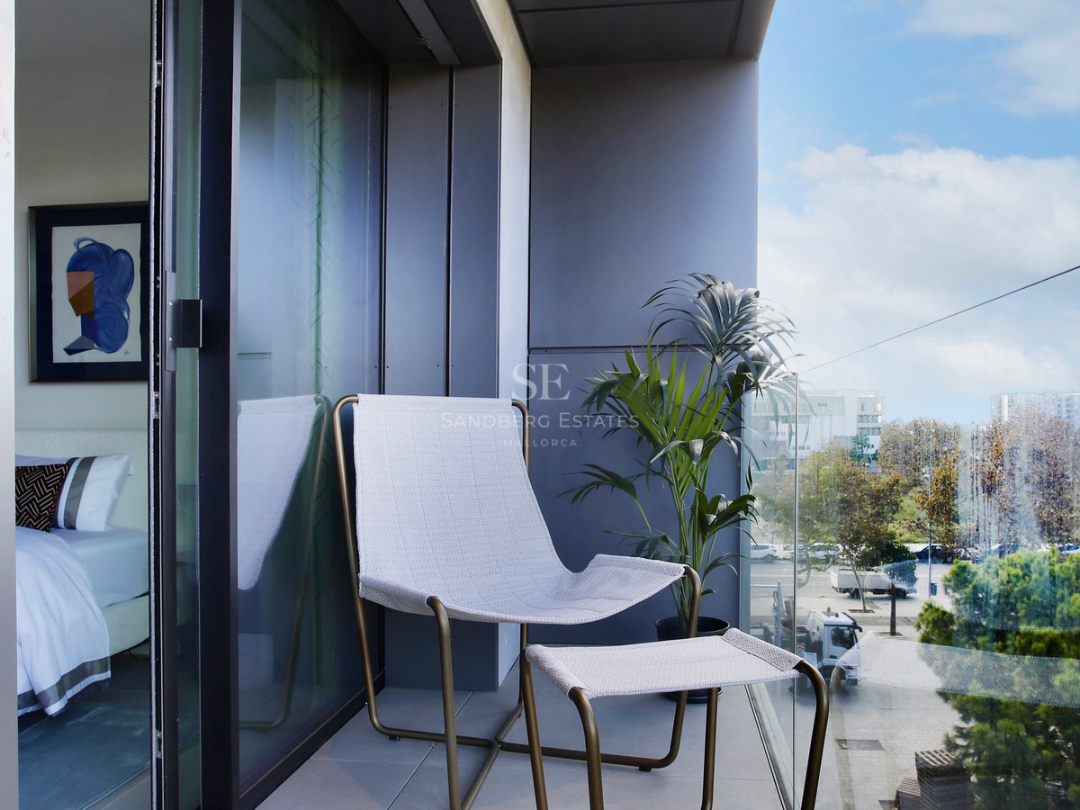Contemporary balcony featuring a designer lounge chair, glass balustrade, and floor-to-ceiling sliding glass doors.
