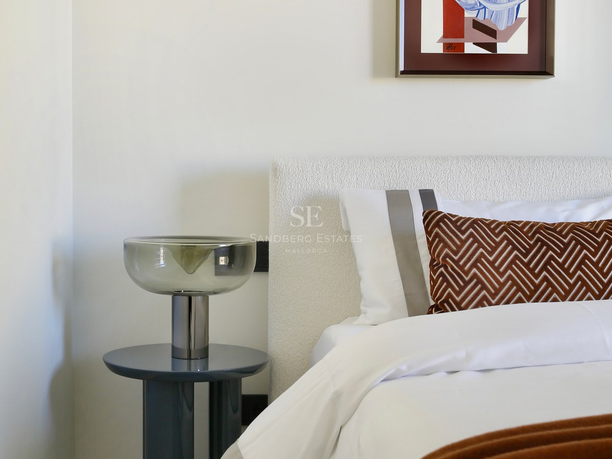 Close-up of a white bouclé headboard, designer glass lamp on a blue side table, and abstract wall art.