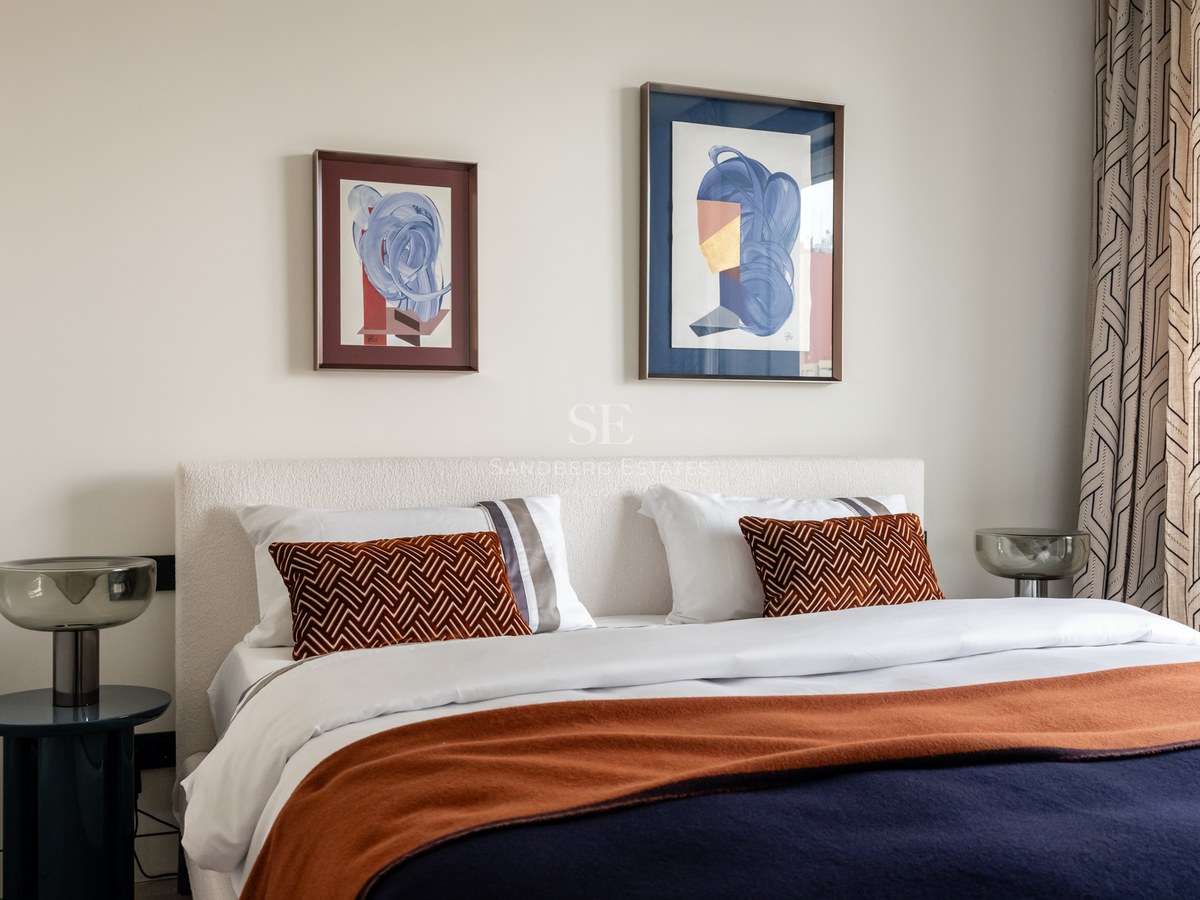 Modern bedroom featuring a white bouclé headboard, navy and terracotta bedding, and abstract artwork above the bed.