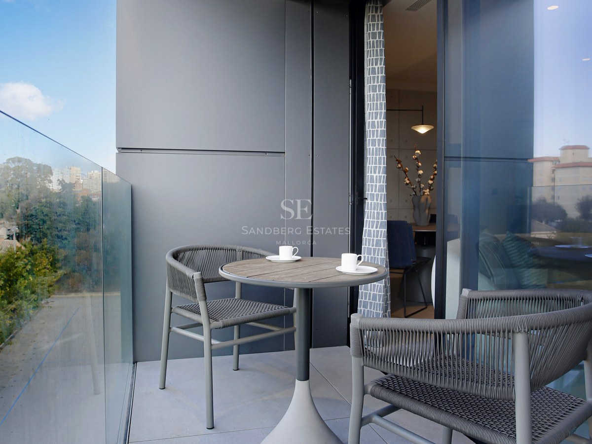 Modern balcony featuring a glass balustrade, two grey woven chairs, and a round pedestal table.