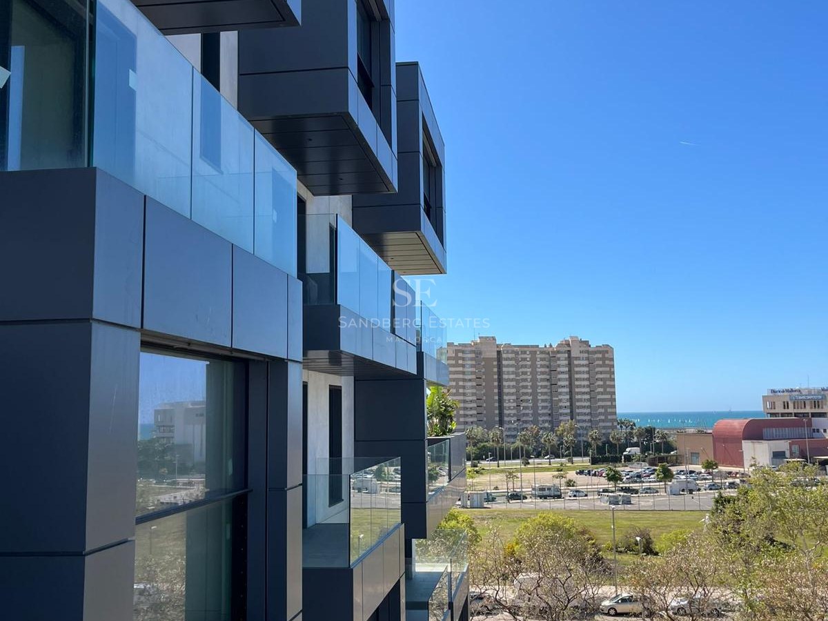Modern dark grey modular facade with glass balconies overlooking an urban park and the Mediterranean Sea.