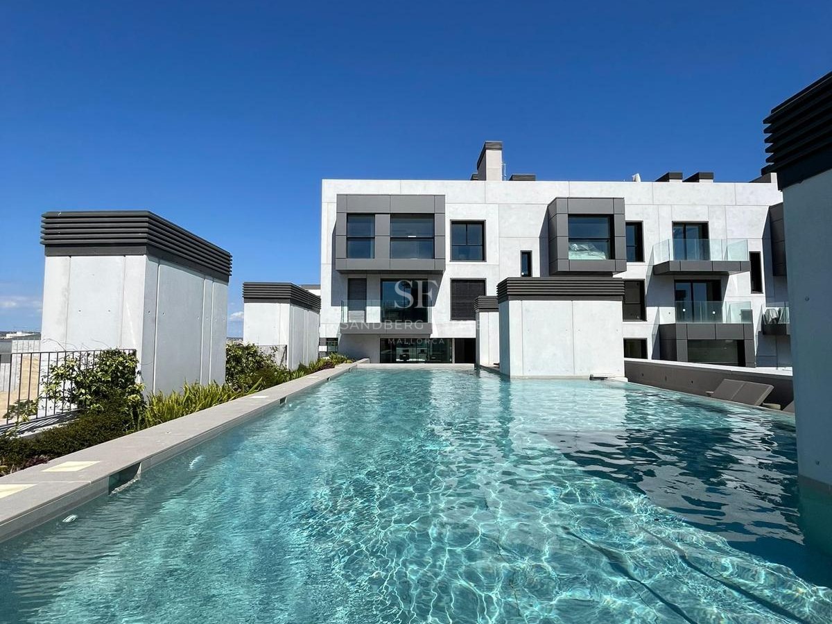 A long turquoise rooftop swimming pool with stone edges in front of a white and grey contemporary apartment building.