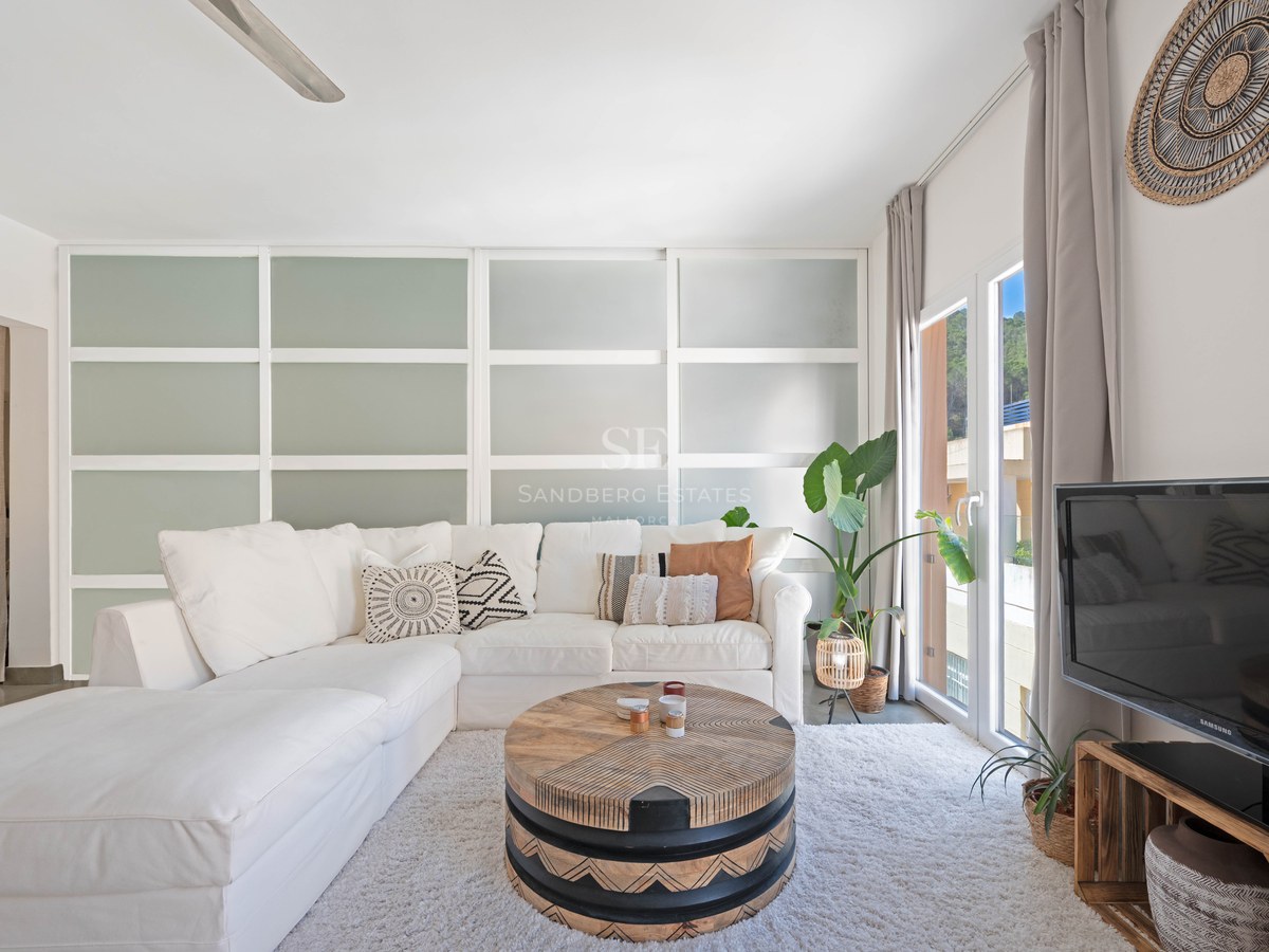 Helles Wohnzimmer mit weißem L-Sofa, geschnitztem Holztisch und Schiebetüren aus Milchglas.
