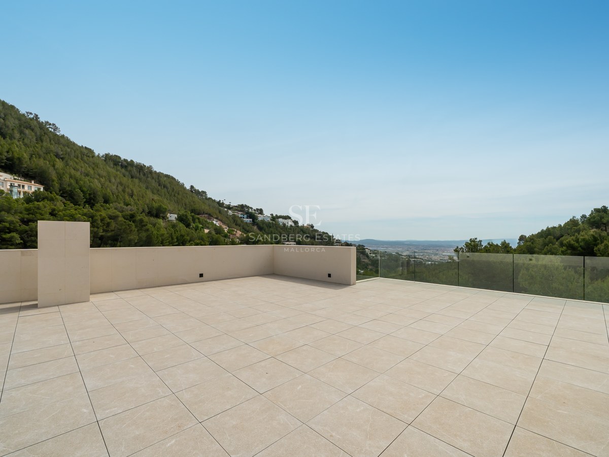 Amplia terraza de piedra natural con barandilla de cristal y vistas a colinas verdes y cielo despejado.