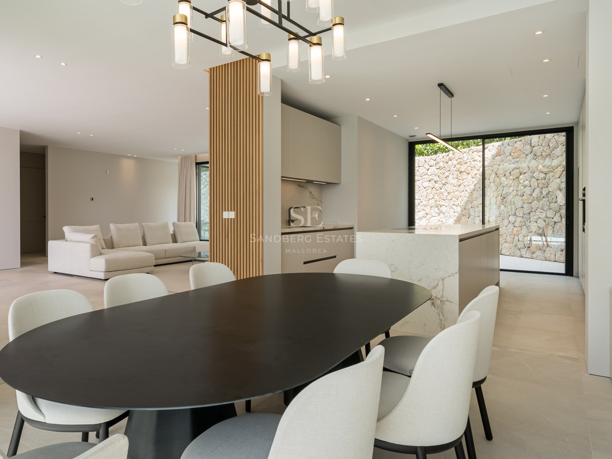 Comedor contemporáneo con mesa negra, sillas blancas, isla de cocina de mármol y pared decorativa de madera.