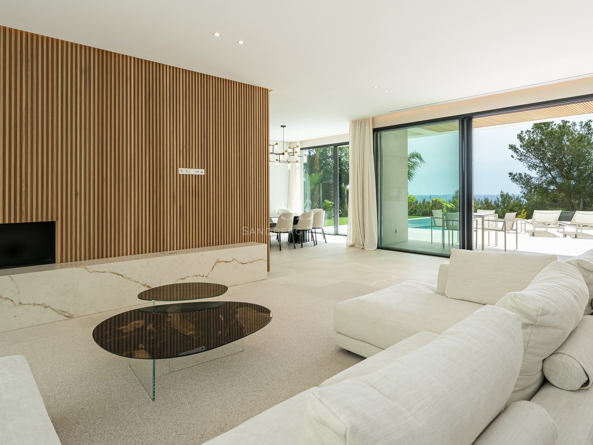 Salón contemporáneo con pared de listones de madera, chimenea de mármol y ventanales que dan a una terraza con piscina.