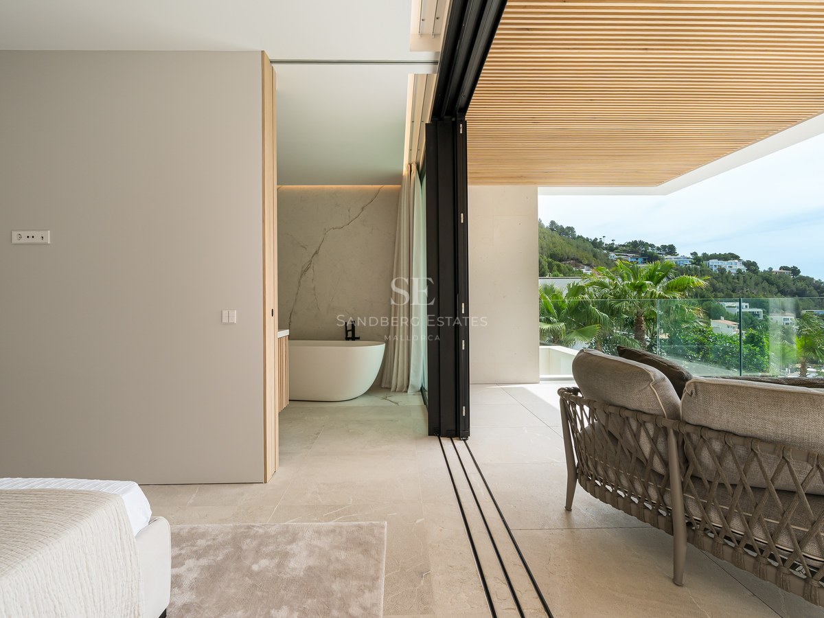 Dormitorio de lujo con bañera exenta y grandes ventanales que abren a una terraza con vistas a las colinas.