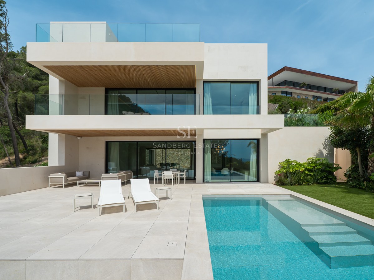 Vista trasera de una villa contemporánea de tres plantas con piscina turquesa, terraza de piedra y jardín.