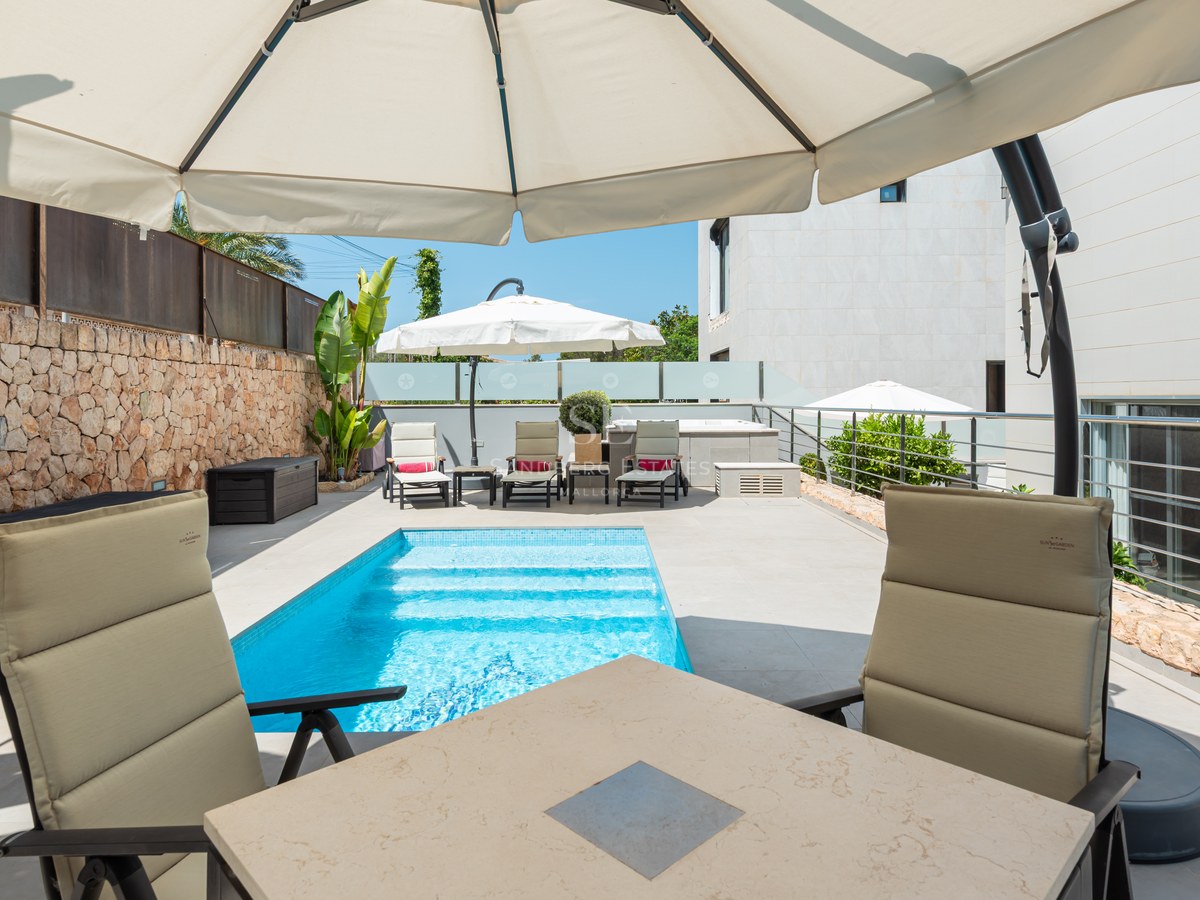 Piscina turquesa en terraza moderna con pared de piedra natural, tumbonas y sombrillas bajo el sol.