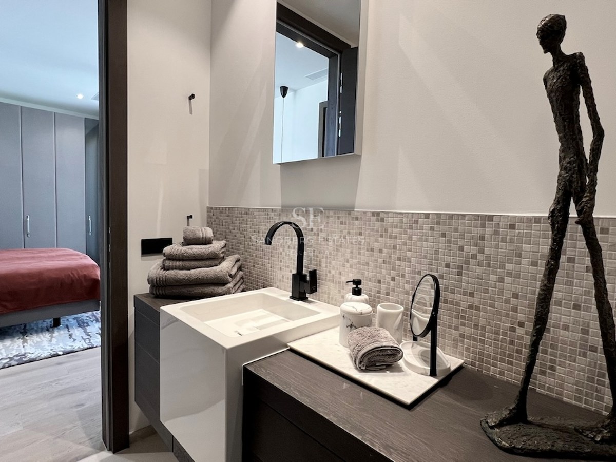 Exterior de villa moderna con piscina infinita, tumbonas, y vistas al mar. Diseño minimalista con líneas limpias y amplias ventanas.