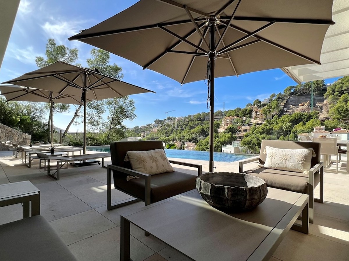 Vista del salón con piscina infinita y terraza. Arquitectura moderna, grandes ventanales, suelo de piedra y muebles de diseño.