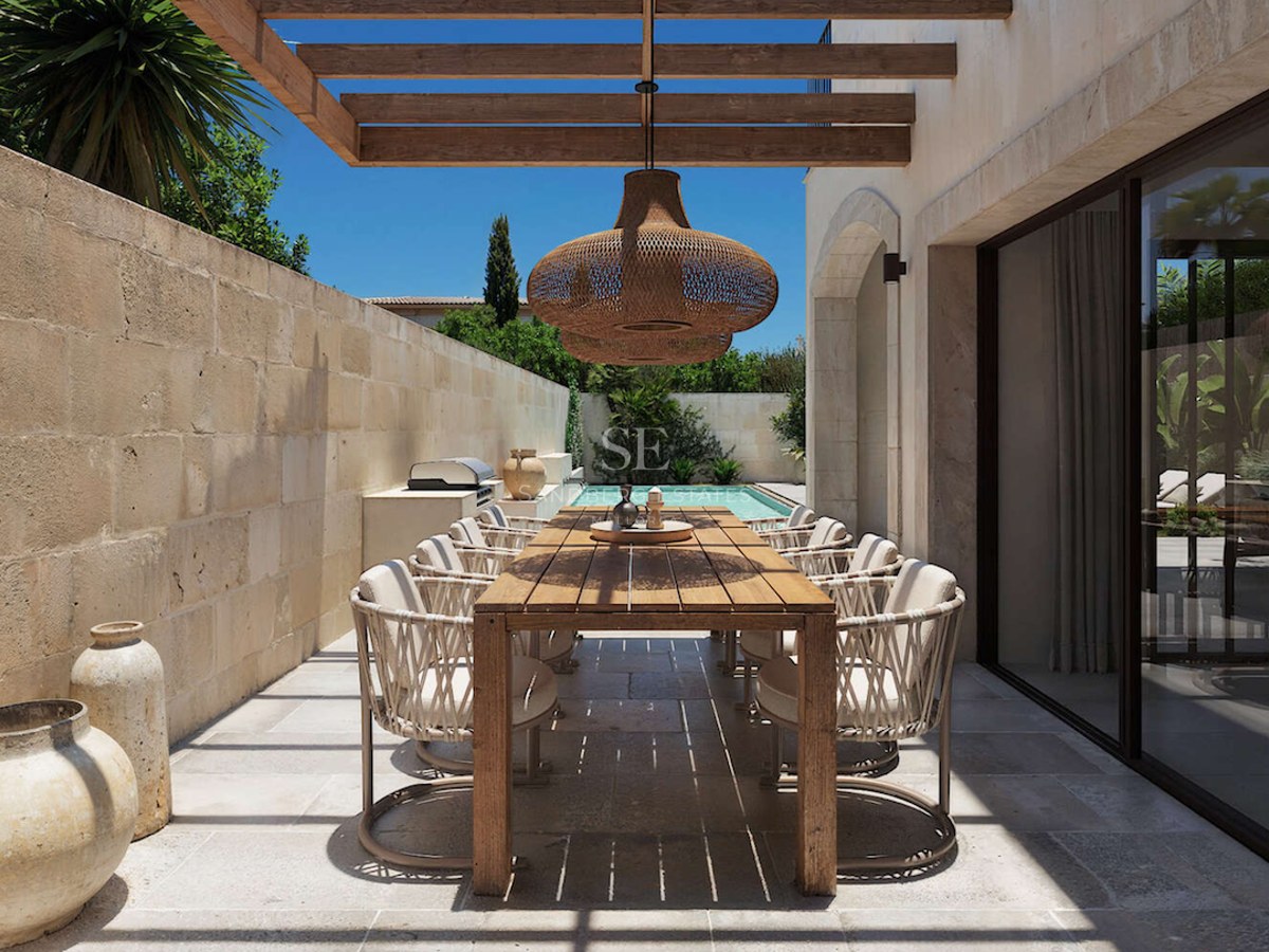Espace repas extérieur sur une terrasse en pierre avec table en bois, pergola et petite piscine en arrière-plan.