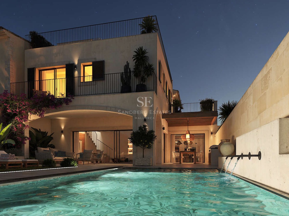Vue nocturne d'une villa de luxe avec piscine éclairée, jets d'eau, murs en pierre et ciel étoilé.