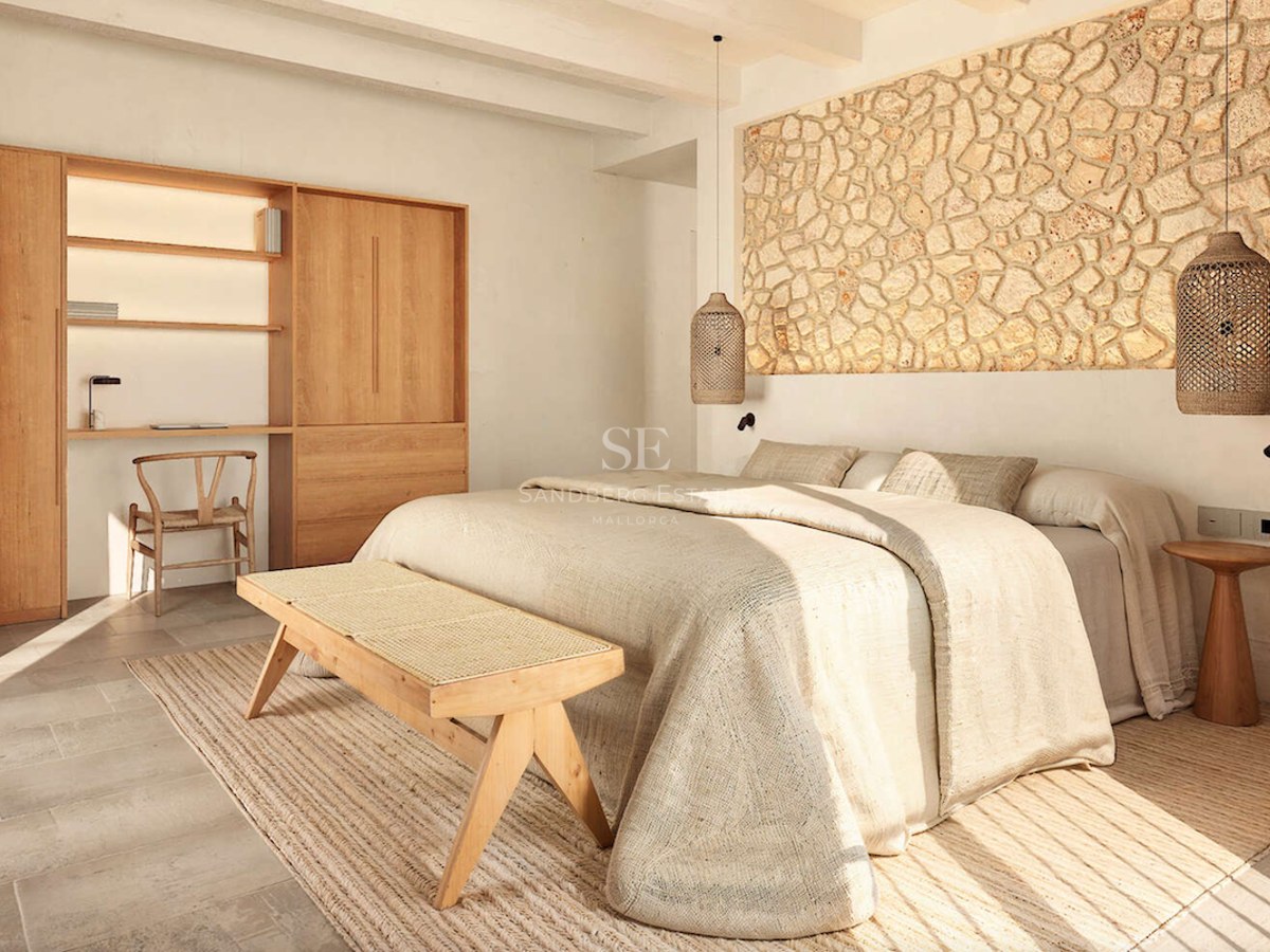 Chambre avec mur en pierre naturelle, bureau en bois et literie en lin sous une lumière naturelle vive.