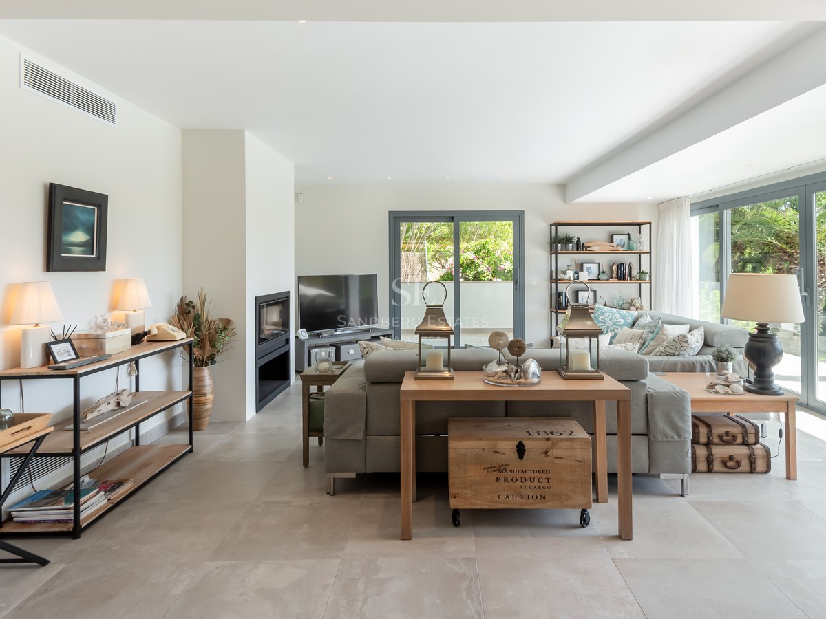 Spacious modern living room with grey sofa, large glass doors to garden, tile floors, and a built-in fireplace.
