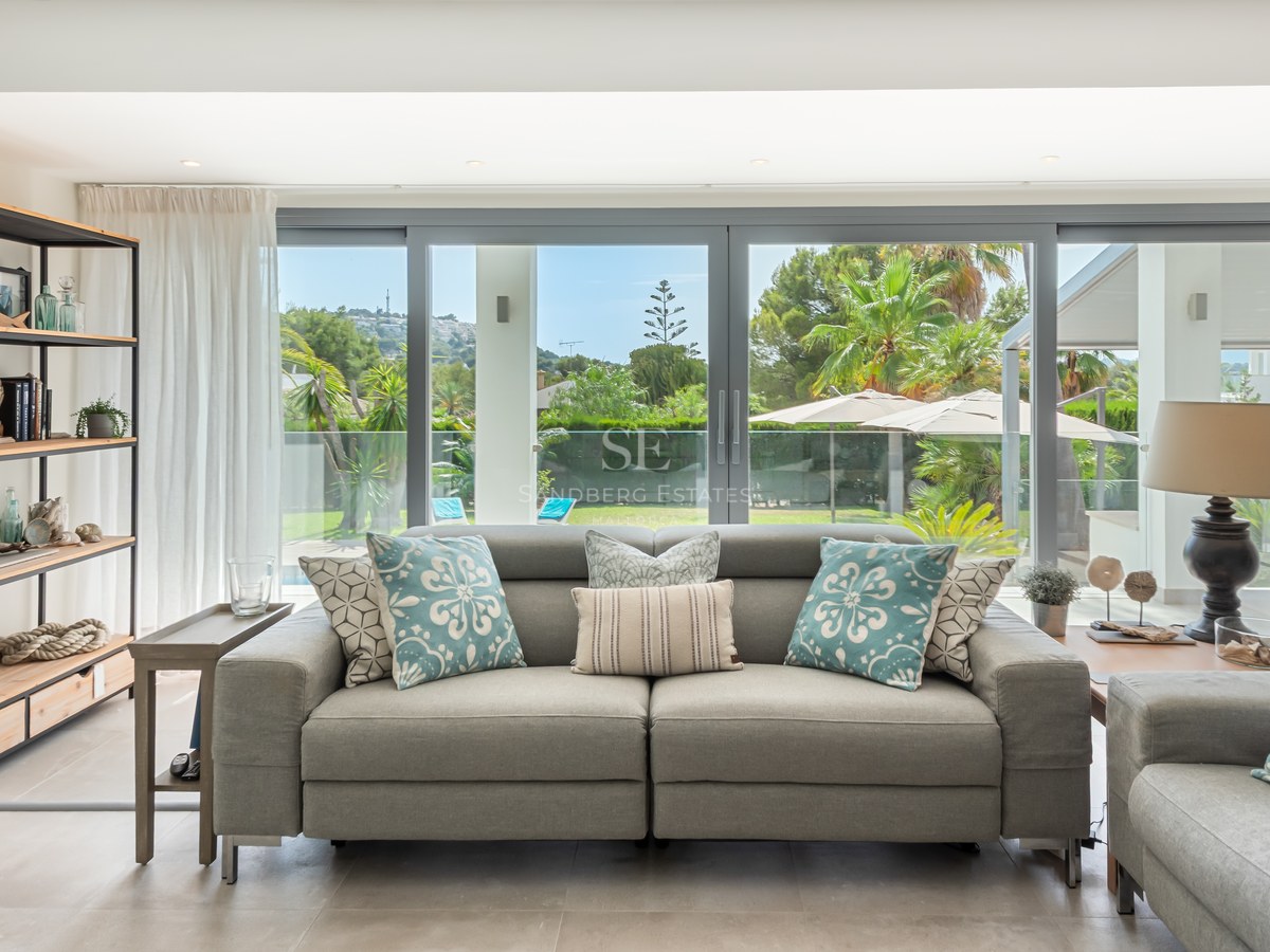 Modern grey sofa and industrial shelving in a bright living room with floor-to-ceiling glass doors opening to a garden.