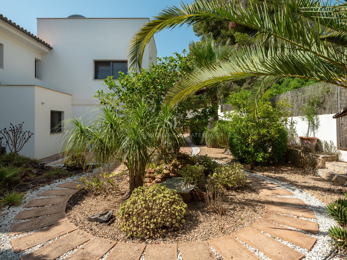 Circular stone pathway in a Mediterranean garden with palm trees and a white modern villa in the background.