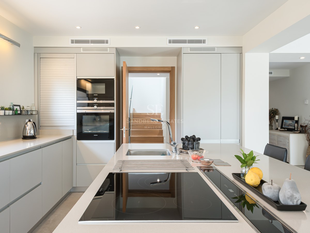 Contemporary kitchen featuring a large white island with induction hob, grey cabinetry, and built-in Siemens ovens.