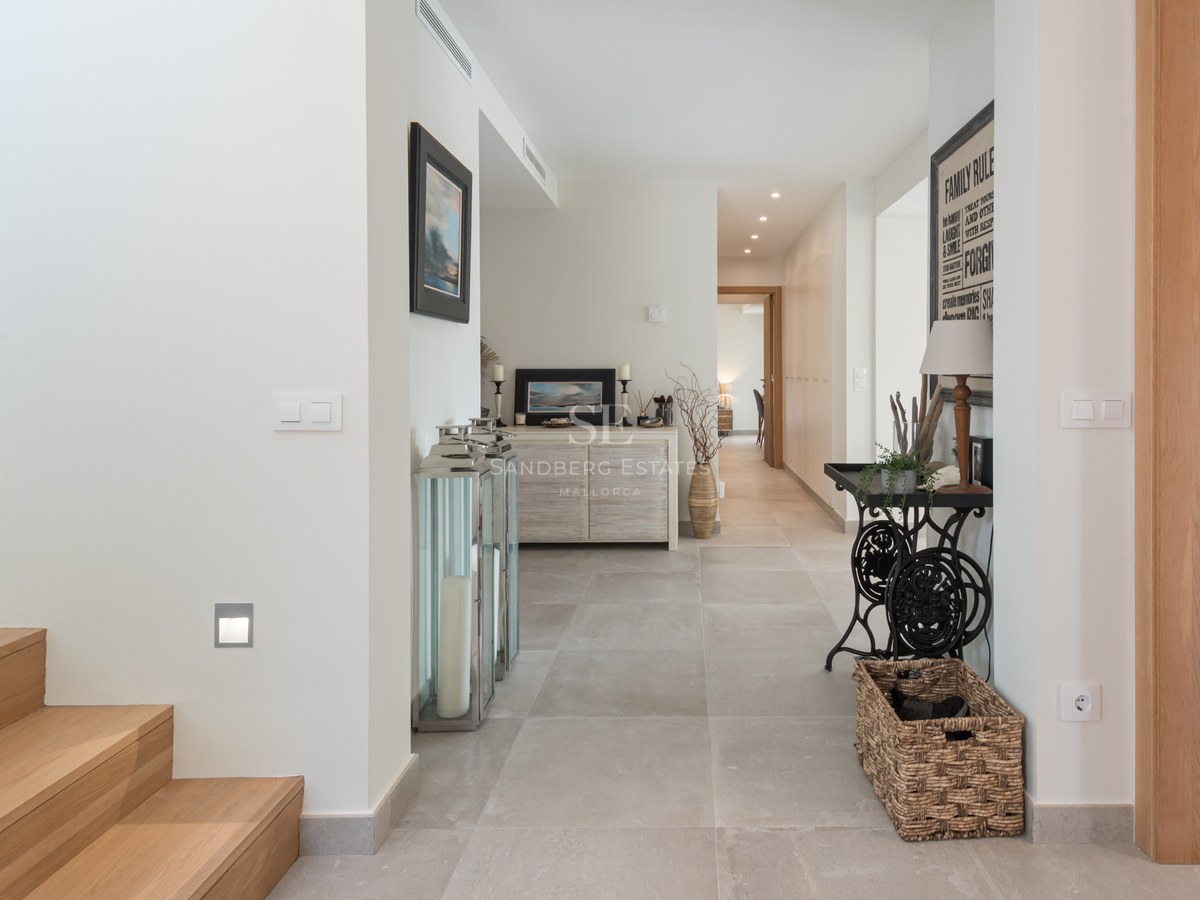 Bright entrance hallway with light wood stairs, stone tile floor, and decorative furniture in a contemporary villa.