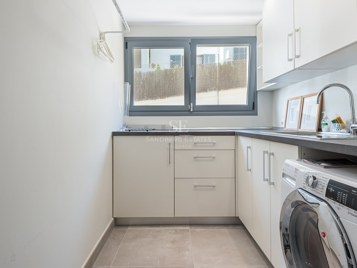 Utility room featuring white cabinetry, a grey countertop, chrome sink, and integrated washing machine under a window.