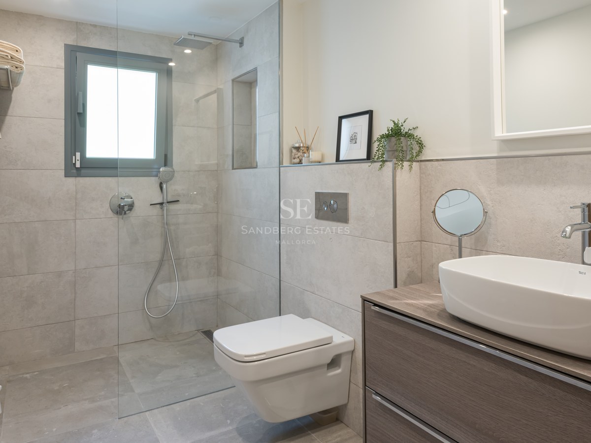 Modern bathroom featuring a glass walk-in shower, wall-hung toilet, and wooden vanity with a white vessel sink.