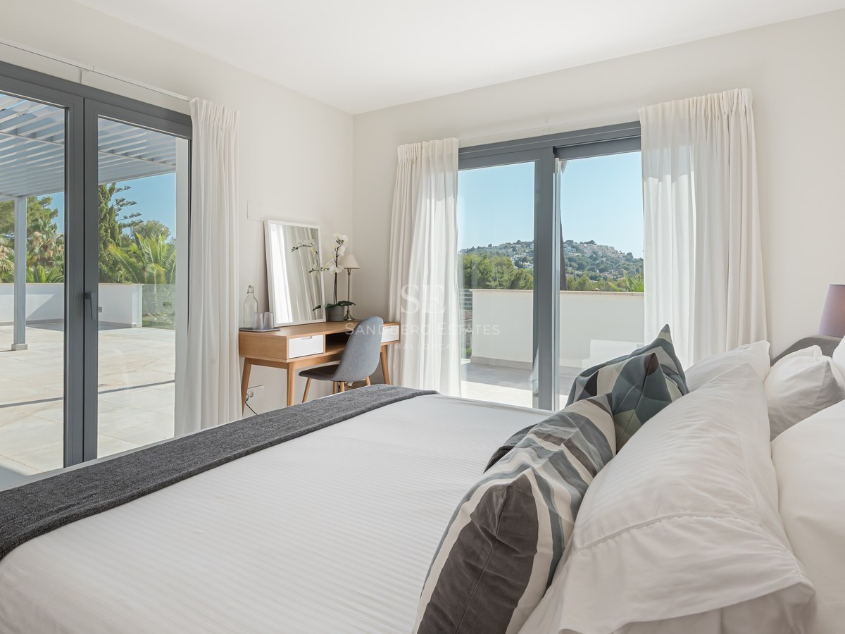 Bright contemporary bedroom with large glass doors opening onto a spacious tiled terrace with hillside views.