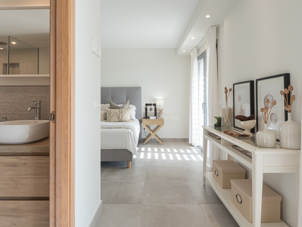 Modern master bedroom with grey bed and ensuite bathroom featuring a vessel sink and wooden vanity.