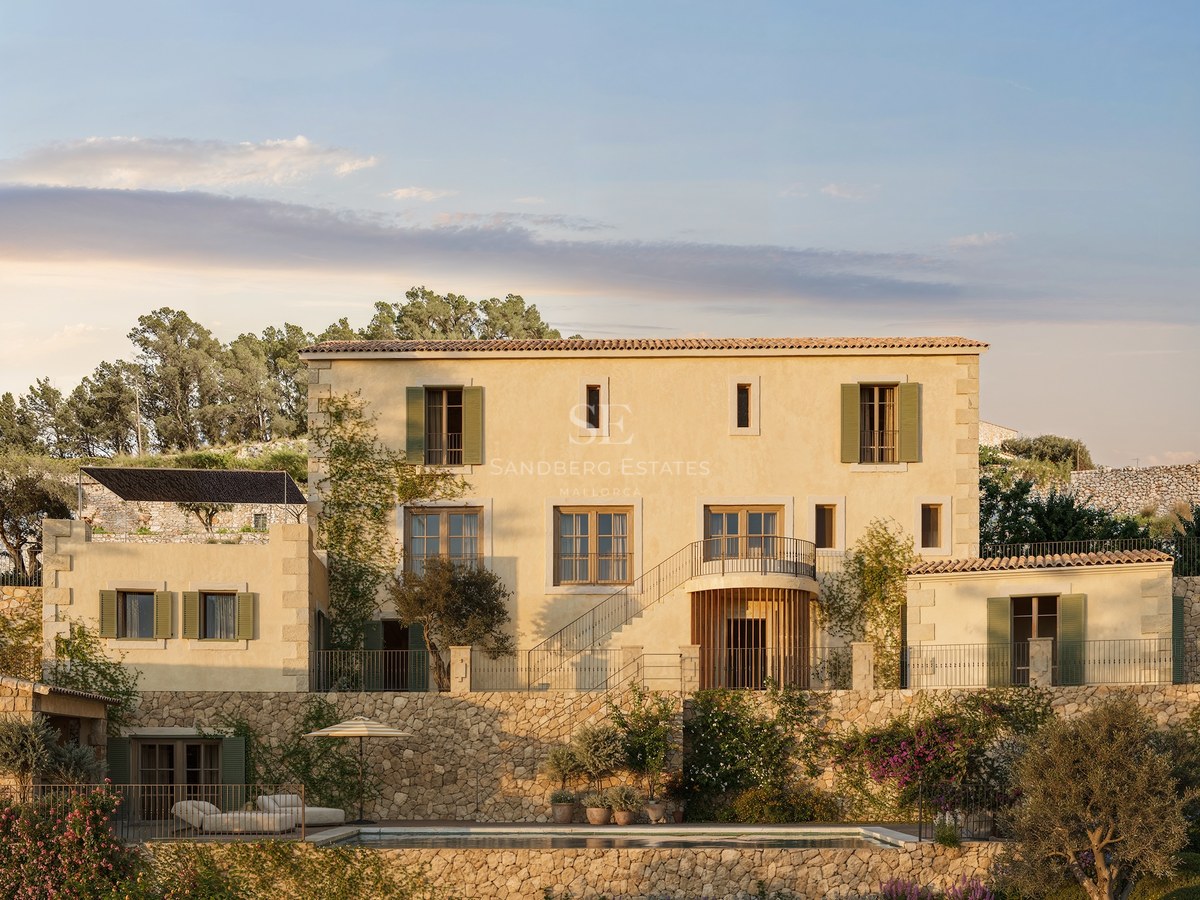 Villa méditerranéenne de trois étages avec façade ocre, murs en pierre, volets verts et piscine dans un jardin en terrasses.