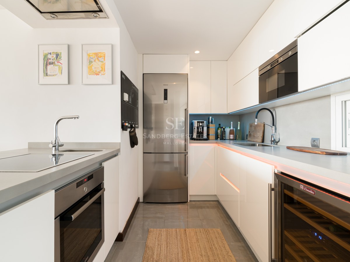 Cocina contemporánea blanca con electrodomésticos de acero inoxidable, vinoteca y encimeras de piedra gris.