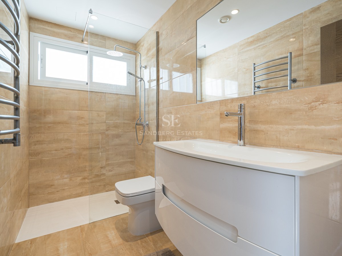 Baño contemporáneo con azulejos beige, lavabo blanco, ducha de cristal y toallero calefactable.