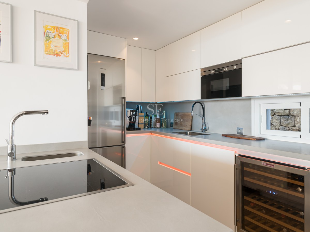 Cocina contemporánea blanca con armarios sin tiradores, vinoteca integrada y electrodomésticos Siemens de acero inoxidable.