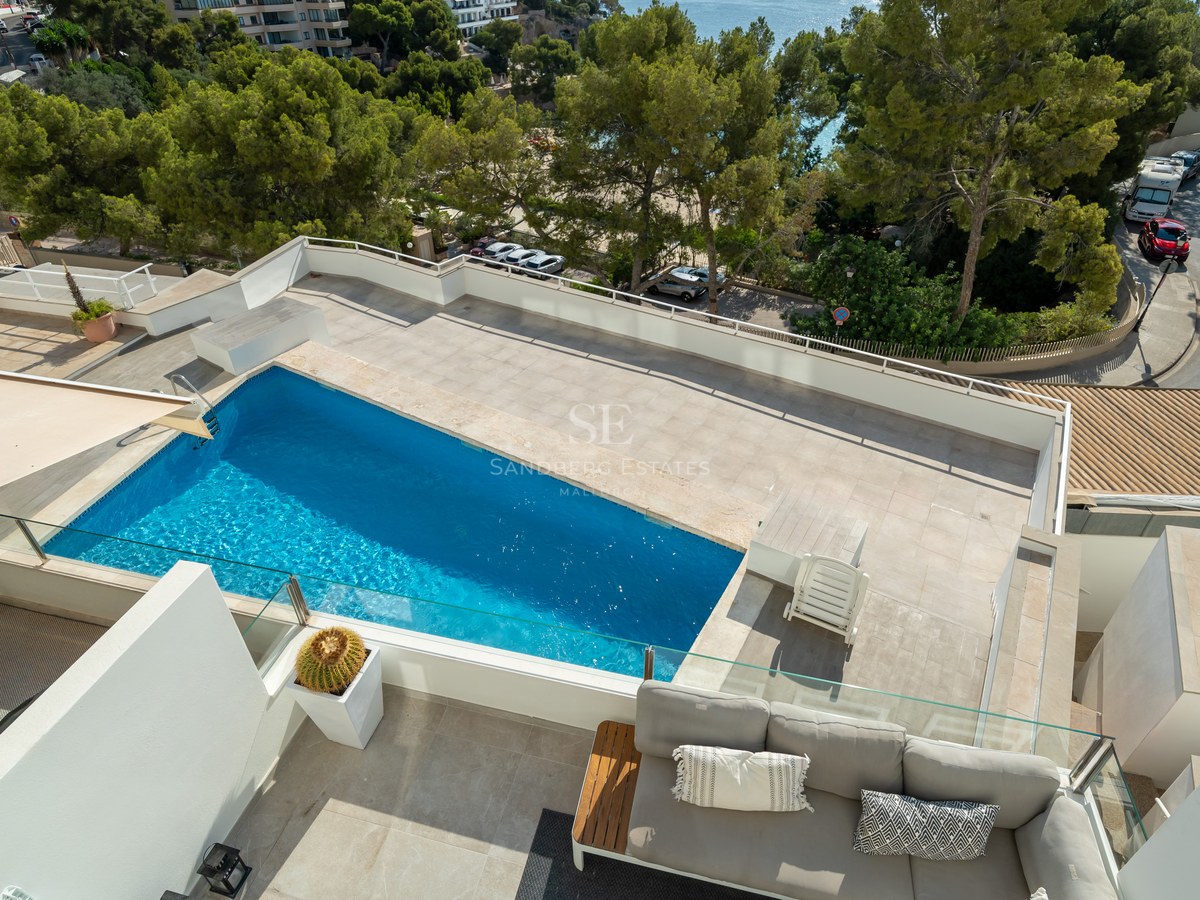 Terraza en la azotea con piscina azul, sofás de exterior y barandillas de cristal con vistas al entorno costero.