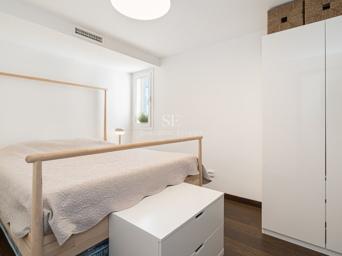 Habitación luminosa con estructura de cama de madera clara, armarios blancos y suelo de madera oscura.