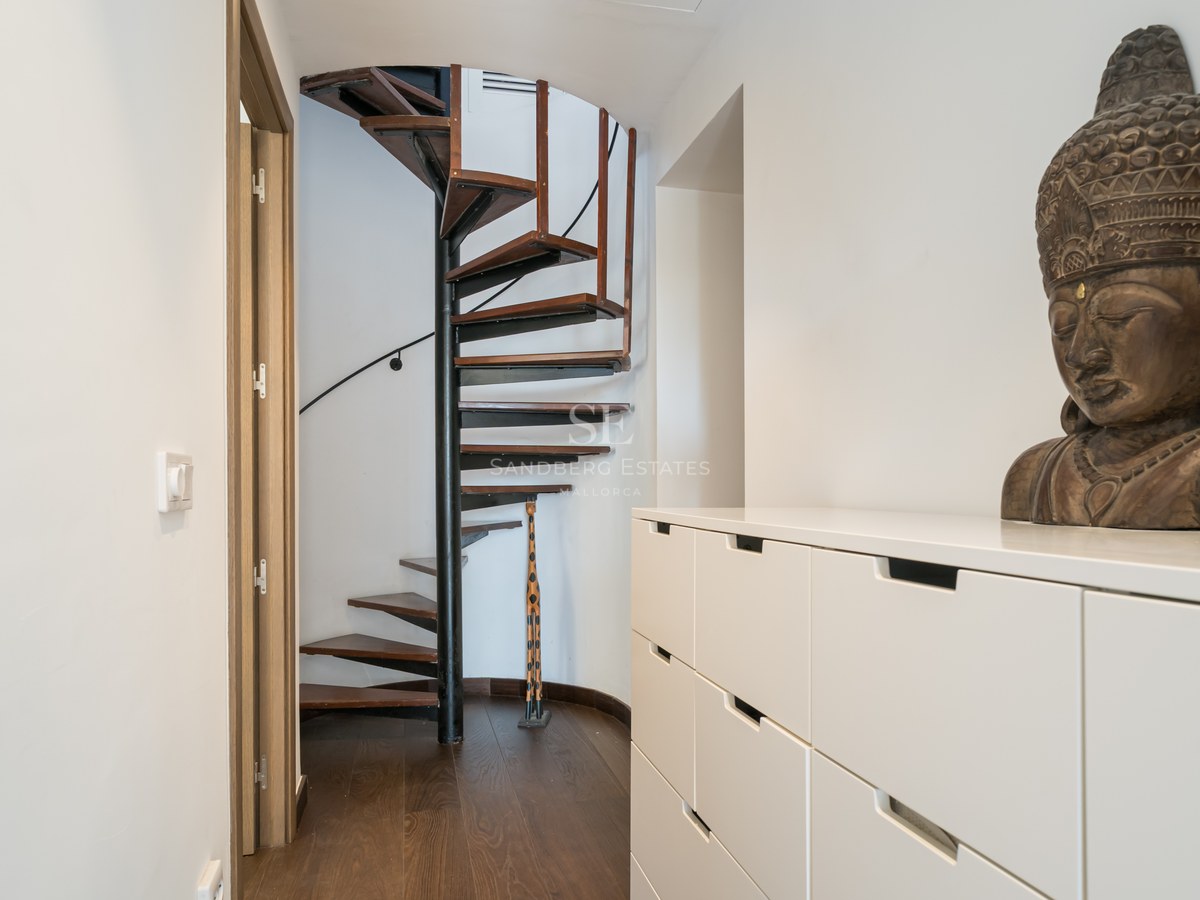 Pasillo moderno con escalera de caracol de madera oscura, mueble blanco y un busto de Buda decorativo.